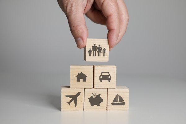 Hand arranging wooden blocks with car insurance, house insurance, travel insurance and boat insurance icons.