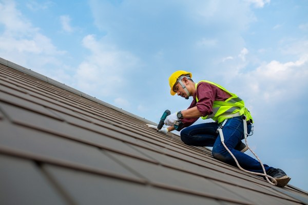 Construction worker fixing roof tiles with electric drills