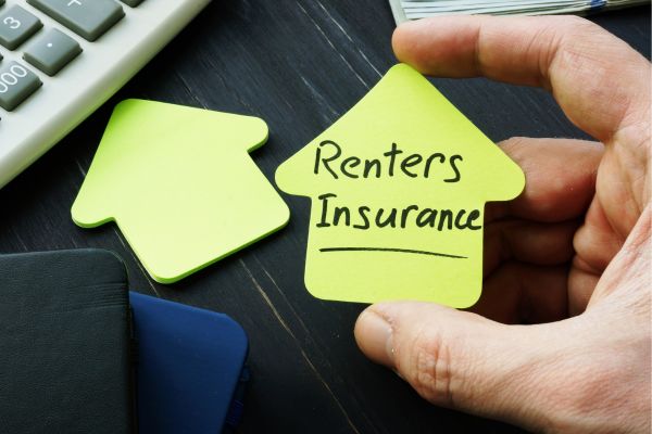 A hand holding a house shape sticky note with the text “Renters Insurance” on it.