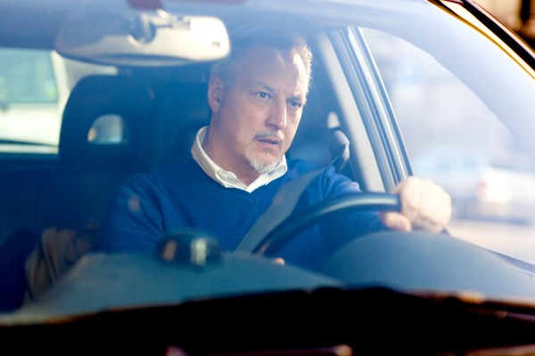 Unhappy male driver holding hands on steering wheel and looking at road with anxiety